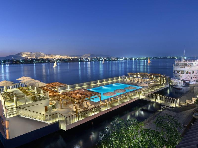 Vista notturna di una lussuosa nave-hotel con piscina illuminata e terrazza sul lungomare.