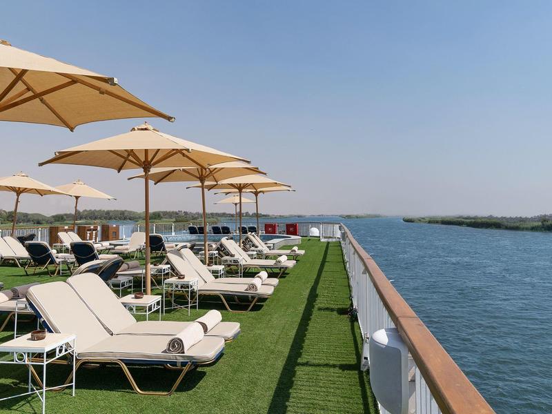 Lettini e ombrelloni su una terrazza accanto all'acqua sotto un cielo limpido.