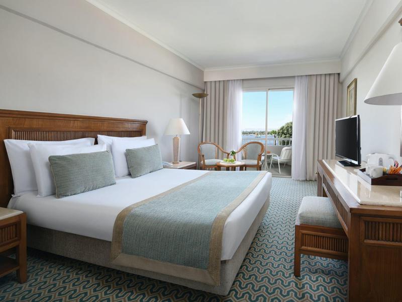 Camera d'hotel elegante con letto matrimoniale, arredi in legno chiaro e vista mare dalla finestra.