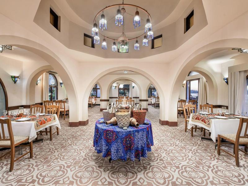 Sala da pranzo elegante con tavoli intorno a un buffet centrale sotto volte bianche.