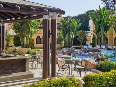 Innenhof eines Hotels mit Pool, Liegestühlen, Pflanzen und Sitzbereich bei Sonnenlicht.