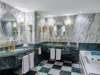 Luxusní koupelna se zeleným mramorem, vanou, umyvadly a oválnými zrcadly.