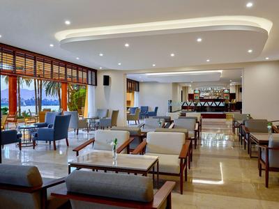 Helles, modernes Hotelrestaurant mit Sitzbereichen und Aussicht auf eine Terrasse mit Palmen.