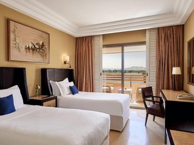 Světý hotelový pokoj se dvěma samostatnými postelemi, balkonem a výhledem ven.