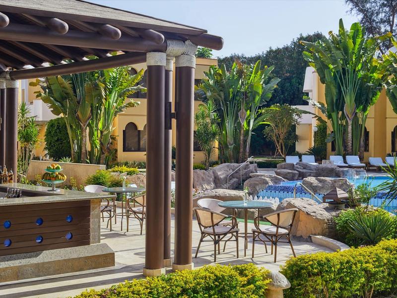 Hotelová terasa s bazénem, stoly, židlemi a bujnou vegetací.