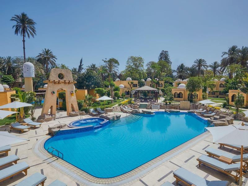 Světlomodrý bazén obklopený lehátky a palmami pod jasnou oblohou.