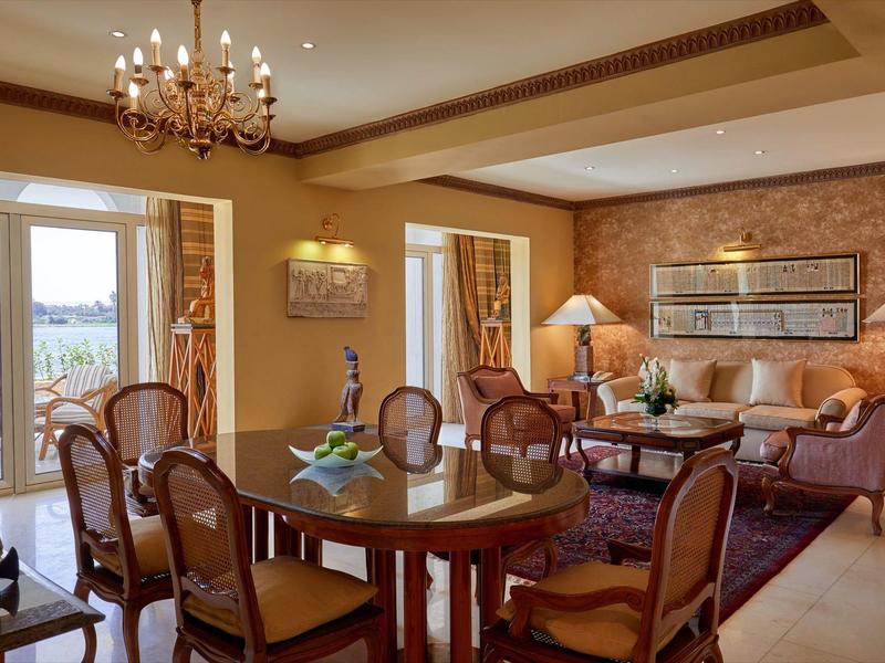 Elegantní hotelový obývací pokoj se dřevěným stolem, židlemi, pohovkami, lampami a výhledem na terasu.