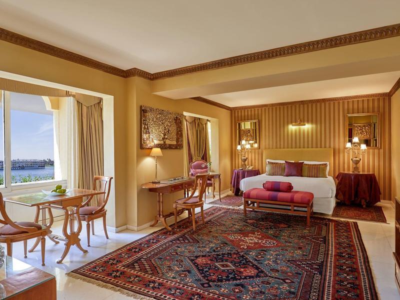 Elegantní hotelový pokoj s velkou postelí, orientálním kobercem a výhledem na moře z terasy.