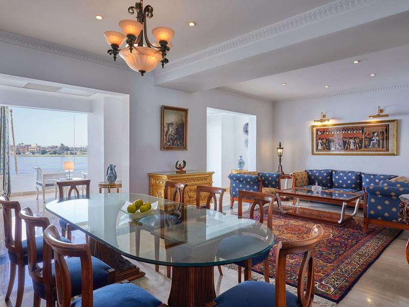 Svět jídelna se skleněným stolem, dřevěnými židlemi, pohovkou a výhledem na moře.