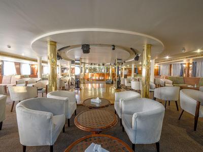 Jasna i przestronna strefa wypoczynkowa hotelu z białymi fotelami i okrągłymi stołami.