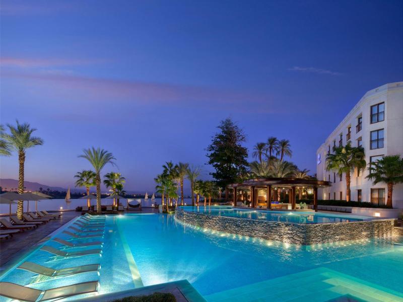 Beleuchteter Hotelpool mit Palmen und Sitzgelegenheiten bei Sonnenuntergang