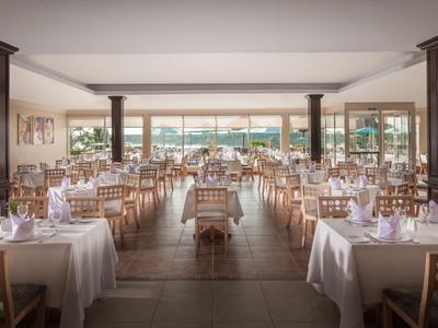 Großes Restaurant mit vielen gedeckten Tischen und Blick auf eine Terrasse und Garten.