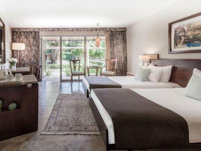 Hell eingerichtetes Hotelzimmer mit zwei Betten, TV und Blick auf einen Garten.