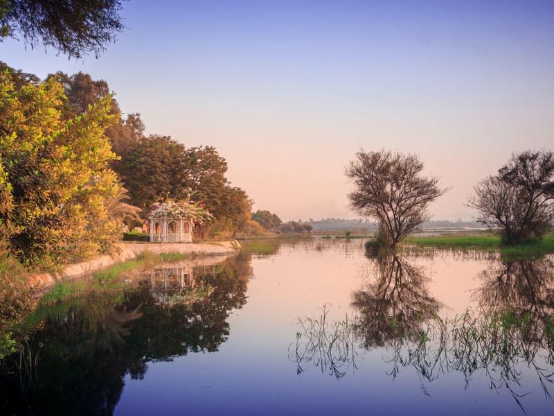 A peaceful lake with trees and a small house on the shore at sunset.