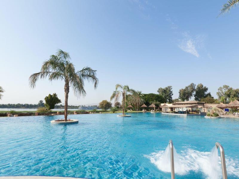 Large outdoor pool with palm trees and sun umbrellas under clear sky.