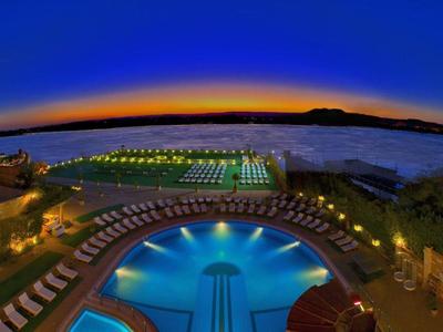 Lit hotel pool at sunset with a view of the sea.