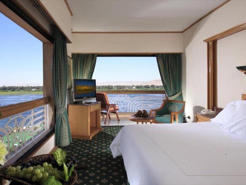 Habitación de hotel con ventana grande y vista al lago con terraza soleada.