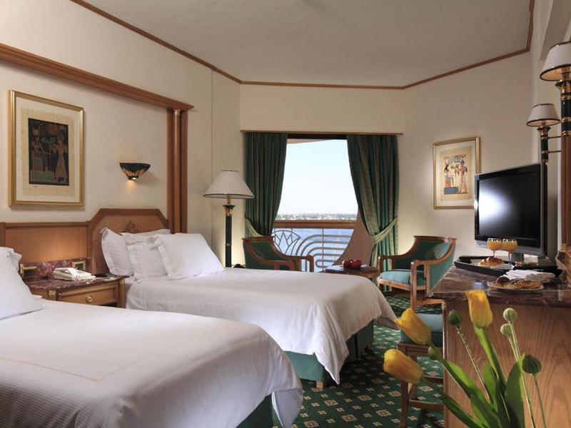 Habitación de hotel con dos camas, escritorio, televisor y vista al agua por la ventana