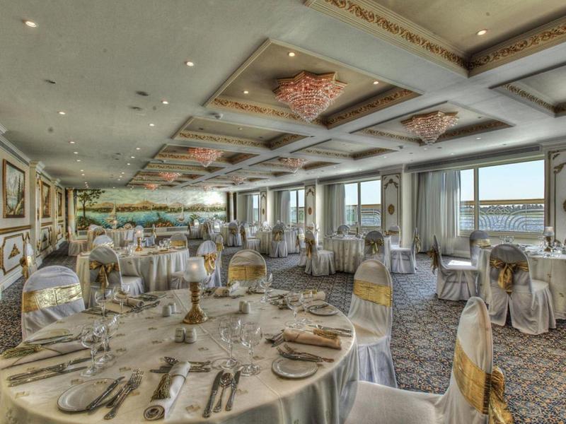 Sala de comedor elegante con mesas decoradas y grandes ventanales con vistas al agua.