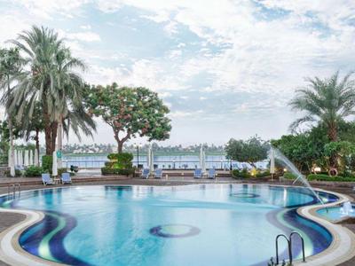 Hotelpool mit Palmen und Seeblick unter bewölktem Himmel