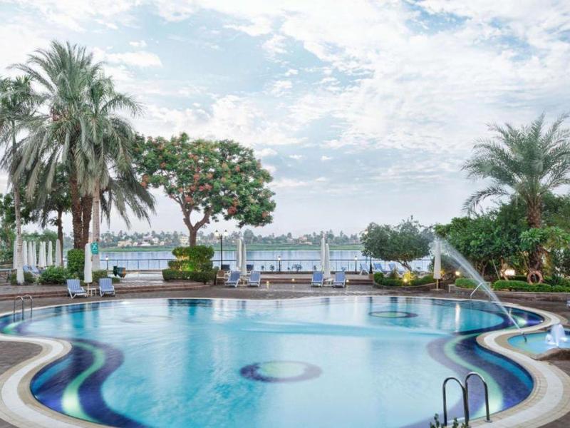 Piscina dell'hotel con palme e vista sul lago sotto un cielo nuvoloso