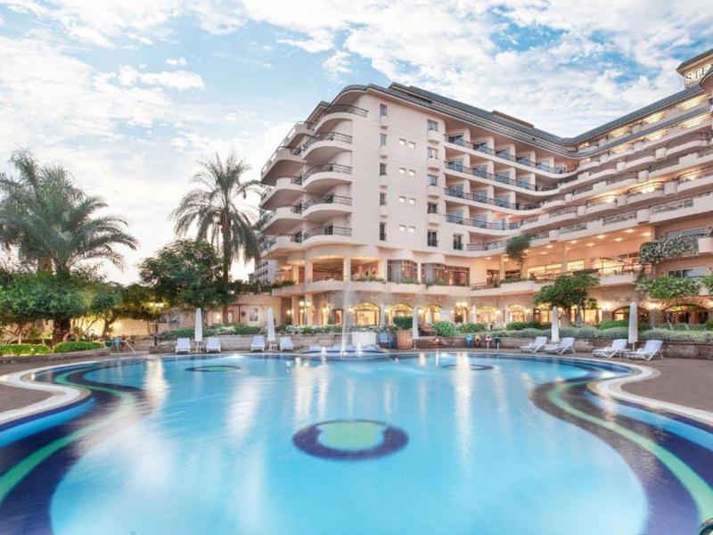 Complesso alberghiero moderno con grande piscina e palme alla luce del giorno