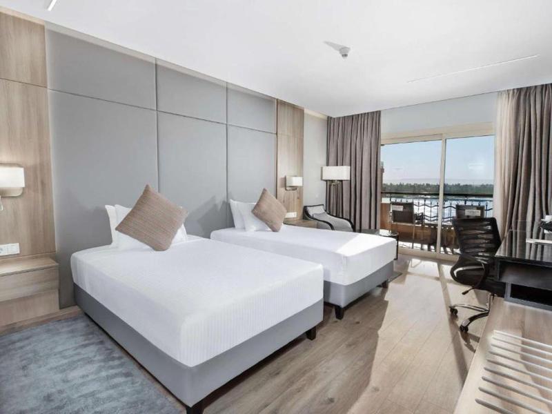 Camera d'hotel moderna con due letti singoli, scrivania e balcone con vista.