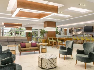 Moderner Hotel-Loungebereich mit bequemen Sesseln, Sofa, Holzelementen und hellem Boden.