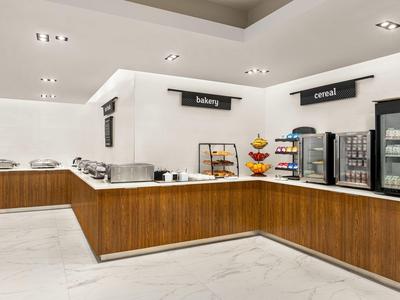 Buffetbereich mit weißen Wänden, Holztheken, Kühlschränken und Beschilderungen für Bakery und Corned.