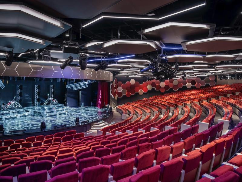 Großer Theatersaal mit roten Sitzreihen und Bühne mit moderner Beleuchtung.