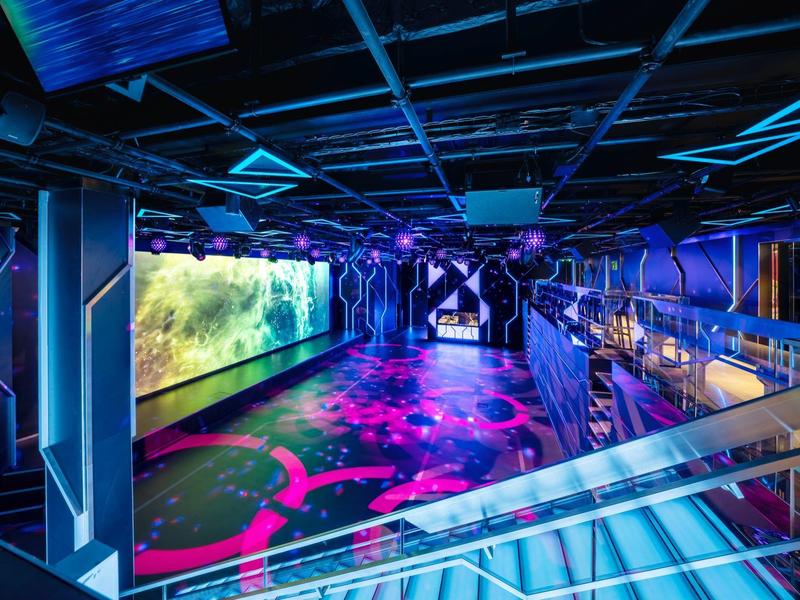 Futuristischer Innenraum mit buntem LED-Beleuchtungsboden und strukturierten Wänden.