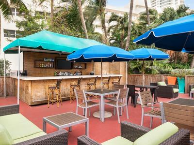 Outdoor-Barbereich mit blauen Sonnenschirmen, Holztresen und Sitzgruppen aus Metall und Rattan.