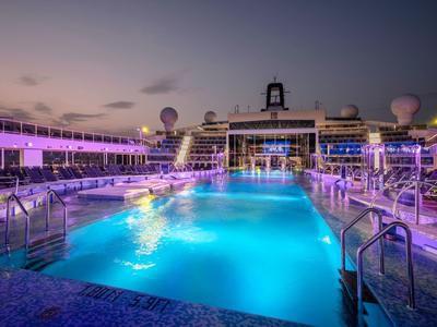 Beleuchteter Pool auf einem Kreuzfahrtschiff bei Sonnenuntergang mit lila Beleuchtung.