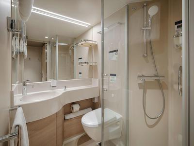 Kompaktes Hotelbadezimmer mit Dusche, WC und Waschbecken mit Spiegel und Haartrockner.