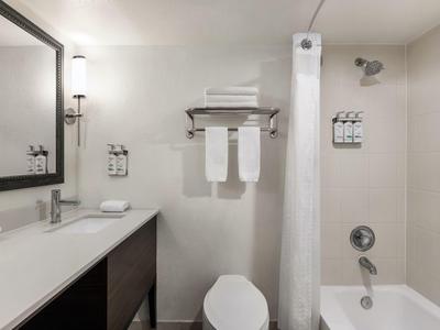 Moderne Badezimmer mit weißer Wand, Waschbecken, Toilette, Badewanne und Handtüchern am Handtuchhalter.