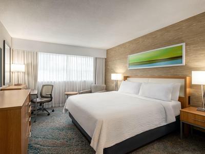 Modernes Hotelzimmer mit großem Bett, Schreibtisch, Stuhl, zwei Nachttischen und Wandbild.