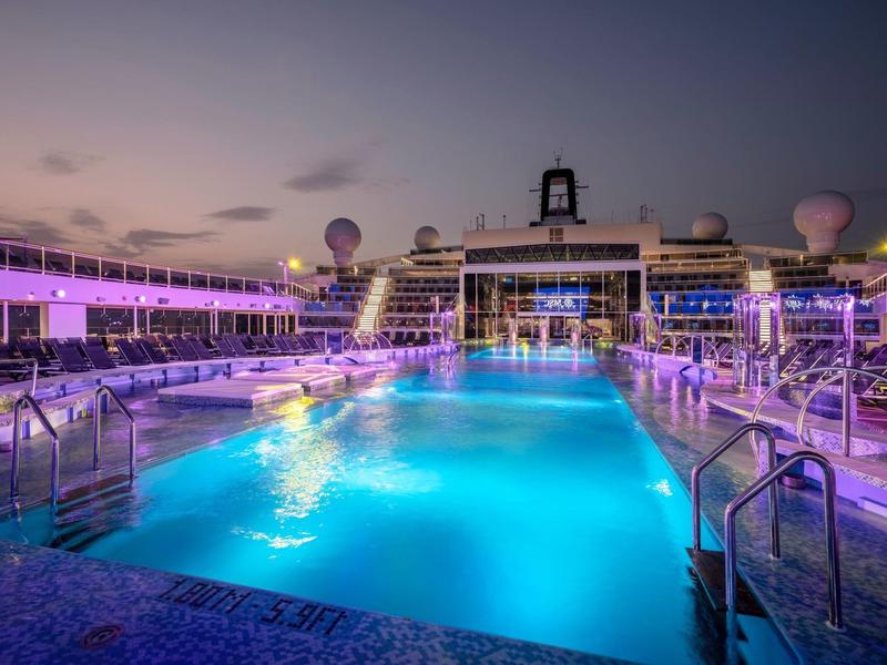 Beleuchteter Pool auf einem Kreuzfahrtschiff bei Sonnenuntergang mit lila Beleuchtung.