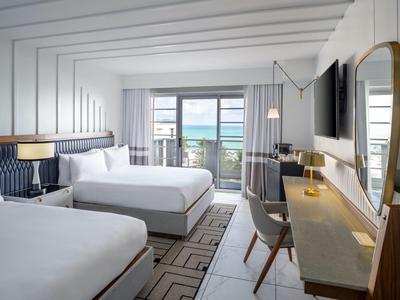 Modernes Hotelzimmer mit zwei Queensize-Betten, Schreibtisch, großem Spiegel und Meerblick durch Balkonfenster.