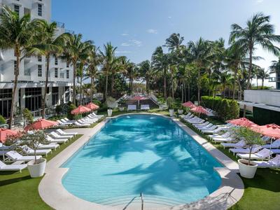 Großer Pool mit blauer Wasserfläche, umgeben von weißen Liegestühlen und roten Sonnenschirmen.