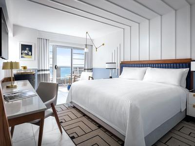 Modernes Schlafzimmer mit großem Bett, Schreibtisch, Meerblick und klaren weißen Linien.