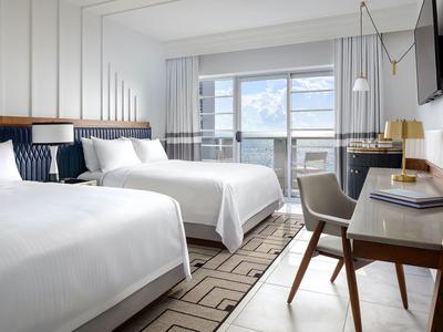 Modernes Hotelzimmer mit zwei Betten, Schreibtisch, Stuhl, großen Fenstern und hellem Holzdekor.