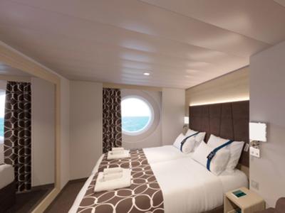 Helles Hotelzimmer mit rundem Fenster, Doppelbett und modernen braunen Vorhängen.