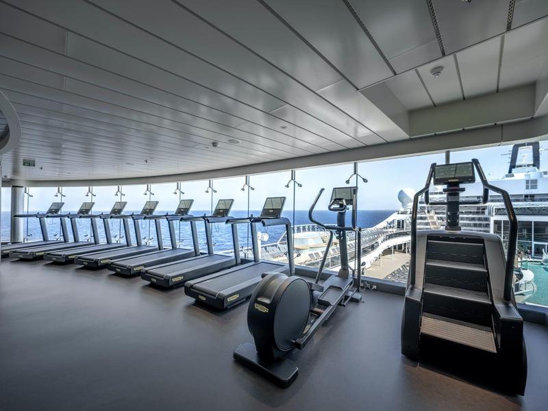 Moderner Fitnessraum mit Laufbändern und Blick auf das Meer durch große Fenster.