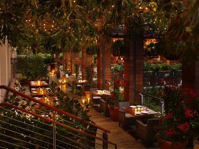 Gemütliche Außenterrasse mit Holzmöbeln, Pflanzen, warmen Lichtern und Tischdekoration bei Dämmerung.