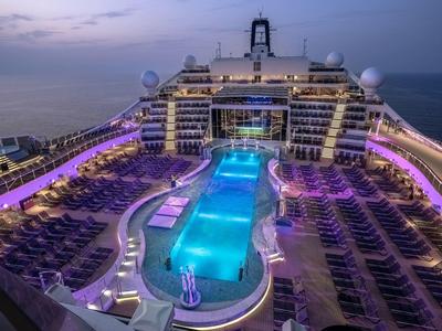 Beleuchteter Poolbereich auf einem Kreuzfahrtschiff bei Dämmerung mit Liegestühlen.