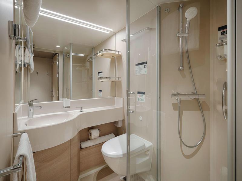 Kompaktes Hotelbadezimmer mit Dusche, WC und Waschbecken mit Spiegel und Haartrockner.