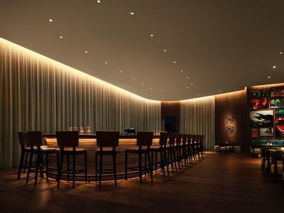 Moderner Barbereich mit langem Holztresen, hohen Stühlen und indirekter Beleuchtung an der Decke.