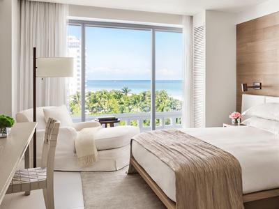 Helles Schlafzimmer mit großem Fenster, Doppelbett mit braunem Überwurf, Sessel und Schreibtisch.