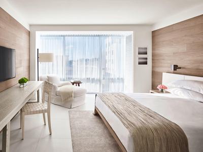 Helles Schlafzimmer mit großem Fenster, Doppelbett, bequemen Sessel und Holzvertäfelung an einer Wand.