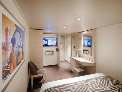 Kompaktes Hotelzimmer mit Bett, Stuhl, Schreibtisch, Spiegel und einem Fernseher an der Wand.